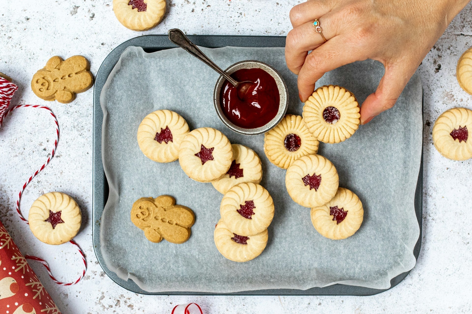 Plateau de biscuits sablés fourrés à la confiture, avec une main en train d’en saisir un, à côté d’un pot de confiture et de biscuits en forme de bonhomme pain d’épices.