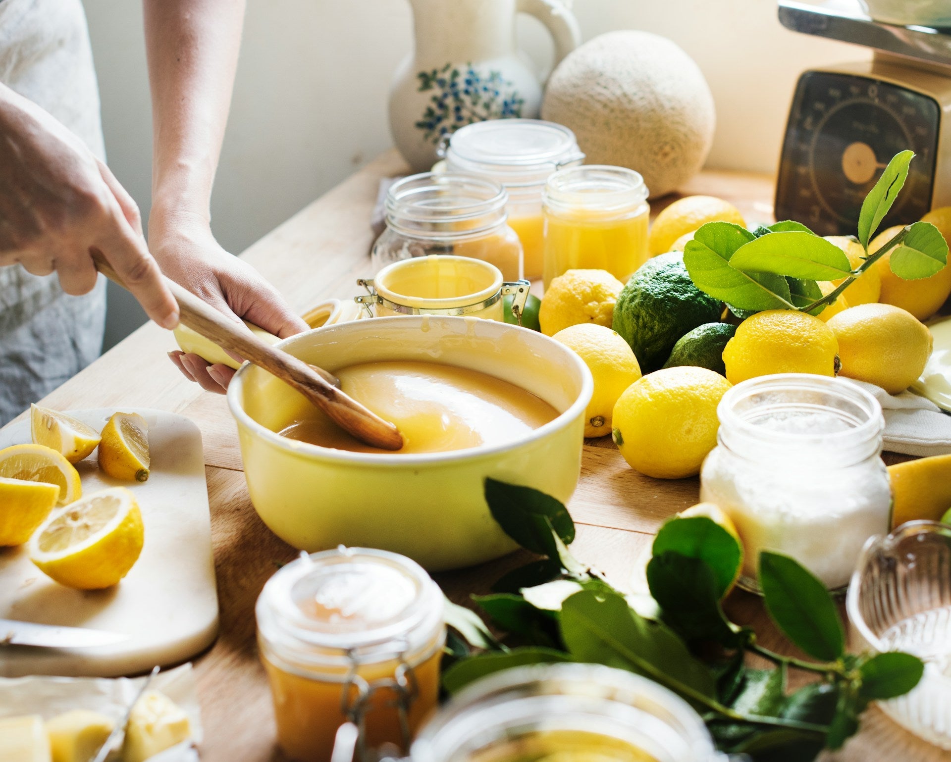 Préparation artisanale de crème de citron dans une cuisine ensoleillée, entourée de citrons frais, pots de confiture et feuillage.