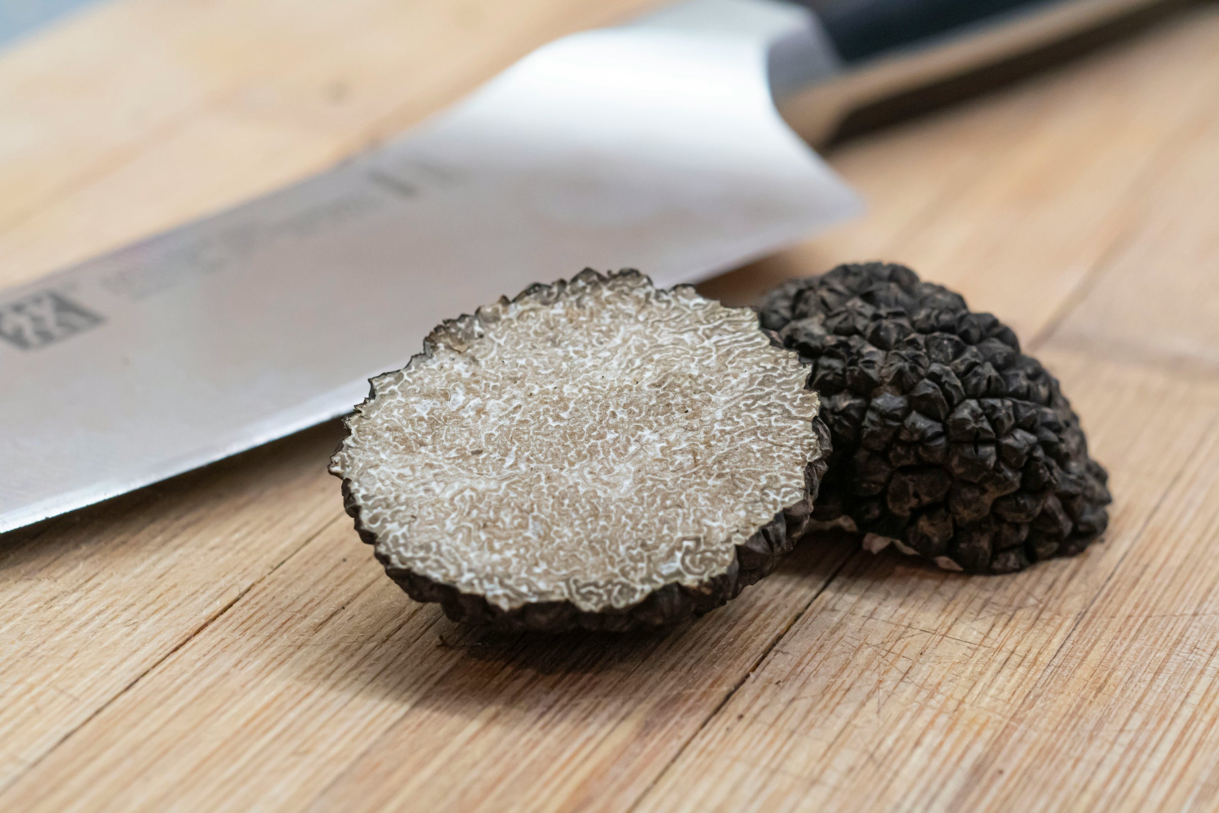 Truffe noire posée sur une planche en bois, avec une moitié tranchée révélant son intérieur marbré, près d’un couteau de cuisine.